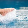 Closeup image of legs and barefoot kicking and splashing water in the pool