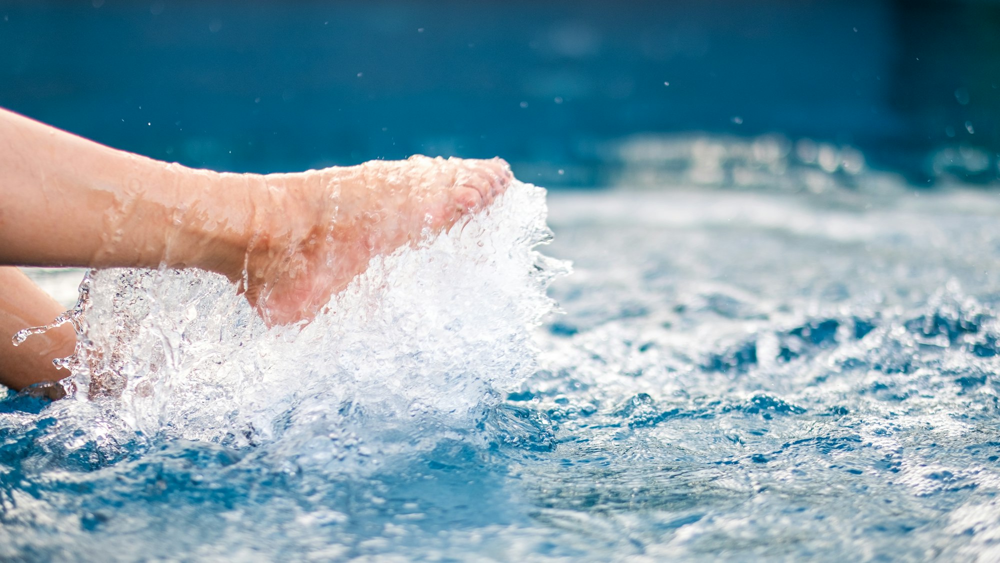 Closeup image of legs and barefoot kicking and splashing water in the pool